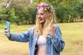 Young woman blonde hair wearing flowers around hair taking selfie photo with smartphone camera in her hands while walking Royalty Free Stock Photo