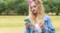 Young woman blonde hair wearing flowers around reading message or social media with smartphone in her hands while walking Royalty Free Stock Photo