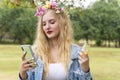 Cheerful young woman blonde hair wearing flowers around reading message or social media with smartphone in her hands while walking Royalty Free Stock Photo