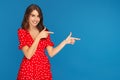 Cheerful young woman with bright smile in red dress pointing fingers away over blue background. Royalty Free Stock Photo