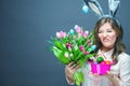 Cheerful young woman with bunny ears and Easter egg basket and tulips Flowers Looking at camera Royalty Free Stock Photo