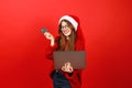 Cheerful young woman in Christmas clothes makes online purchases using a laptop and a credit card on a red background Royalty Free Stock Photo