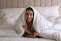 Cheerful young woman covered with warm white blanket lying in bed Royalty Free Stock Photo
