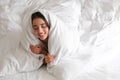 Cheerful young woman covered with warm white blanket lying in bed. Space for text Royalty Free Stock Photo