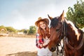 Cheerful young woman cowgirl standing with her horse in village Royalty Free Stock Photo