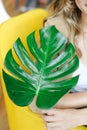 Cheerful young woman embracing a vibrant green monstera plant leaf