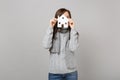 Cheerful young woman in gray sweater, scarf hiding, covering face with paper white house isolated on grey background in