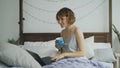 Cheerful young woman having video chat with friends using laptop camera while sitting on bed at home Royalty Free Stock Photo