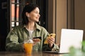 Cheerful Young Woman Holding Credit Card and Smartphone Making Online Shopping While Sitting at a Cafe Table with Laptop Royalty Free Stock Photo