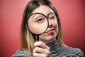 Cheerful young woman looking through magnifying glass at the camera over pink background Royalty Free Stock Photo