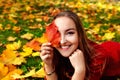 A cheerful young woman lying on the ground, covered with autumn yellow and red leaves, in a beautiful park. She put a maple leaf Royalty Free Stock Photo