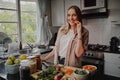 Cheerful young woman in modern kitchen preparing fresh vegetables salad and eating a carrot smiling at the camera Royalty Free Stock Photo