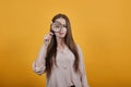 Cheerful young woman in pastel shirt keeping magnifier glass, looking on it