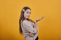 Cheerful young woman in pastel shirt staying sideways, pointing palm aside