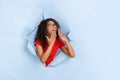 Cheerful young woman poses in torn blue paper hole background, emotional and expressive