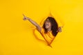 Cheerful young woman poses in torn yellow paper hole background, emotional and expressive