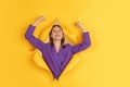 Cheerful young woman poses in torn yellow paper hole background, emotional and expressive