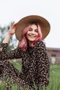 Cheerful young woman with positive smile with colored hair in straw vintage hat in black fashion dress is relaxing on grass on Royalty Free Stock Photo