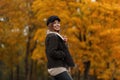 Cheerful young woman with positive smile in a jacket in a trendy hat with a leather bag posing in autumn park on a background of Royalty Free Stock Photo