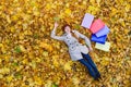 Cheerful young woman with shopping bags tired lying on foliage. Autumn discounts. Top view