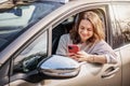 Cheerful young woman sitting in a car in the driver& x27;s seat looking into a smartphone, paying for parking and Royalty Free Stock Photo