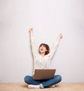 Cheerful young woman sitting on floor with laptop and hands raised Royalty Free Stock Photo