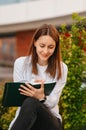 Cheerful young woman is sitting outdoors while writing down some observations. Royalty Free Stock Photo