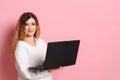 A cheerful young woman standing isolated on a pink background using a laptop computer Royalty Free Stock Photo