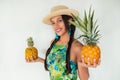 A cheerful young woman in a straw hat holding whole pineapple fruits, looking at the camera, smiling Royalty Free Stock Photo