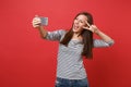 Cheerful young woman in striped clothes doing taking selfie shot on mobile phone showing victory sign isolated on bright Royalty Free Stock Photo