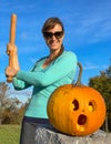 Cheerful young woman is about to smash scared Halloween pumpkin with wooden bat