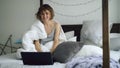 Cheerful young woman using her laptop computer sitting in bed at home Royalty Free Stock Photo