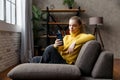 Cheerful young woman using mobile phone while sitting on a sofa at home. Royalty Free Stock Photo