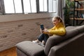 Cheerful young woman using mobile phone while sitting on a sofa at home. Royalty Free Stock Photo