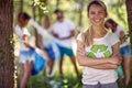 Cheerful young woman volunteer in nature. Group of people cleaning up forest or park doing charity work. Environmentalism, green,