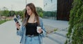 Cheerful young woman is walking on the street and drinks coffee and using smartphone. Woman messaging on phone at street