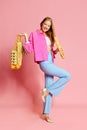 Cheerful young woman wearing jeans, heels holding purchases and baguette over pink background