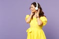 Cheerful young woman in yellow dress keeping eyes closed listen music, putting hands on headphones isolated on pastel Royalty Free Stock Photo