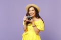 Cheerful young woman in yellow dress, summer hat taking pictures on retro vintage photo camera isolated on pastel violet Royalty Free Stock Photo