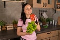 Happy young woman with vegetable on kitchen. Cheerful youthful female enjoying healthy lifestyle while holding bell