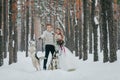 Cheerfull couple with two siberian husky are posed on background of snowy forest. Artwork Royalty Free Stock Photo