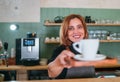 Cheerfully smiling barista female giving white cup aromatic espresso at the coffee shop counter. Happy people, coffee consumption