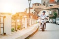 Cheerfully smiling man in sunglasses fast riding the moto scooter on the Sicilian old town streets in the Forza d\'Agro