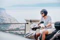 Cheerfully smiling man in helmet and sunglasses fast riding the moto scooter on the Sicilian old town streets on the Ionian