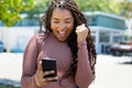 Cheering african american young adult woman with phone receiving message with good news Royalty Free Stock Photo