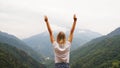 Cheering woman hiker open arms at mountain peak