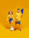 A cheerleader girl and a soccer player in the same uniform are standing, holding the ball with his foot. Boy holding pompons