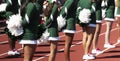 Cheerleaders in green uniforms holding white pom poms behind their backs Royalty Free Stock Photo