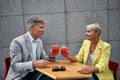 Cheers. Beautiful mature couple in stylish wear drinking cocktails while sitting in cafe outdoors together