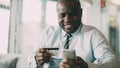 Cheery African American businessman in formal clothes paying online bill keeping credit card and smartphone in his hands Royalty Free Stock Photo